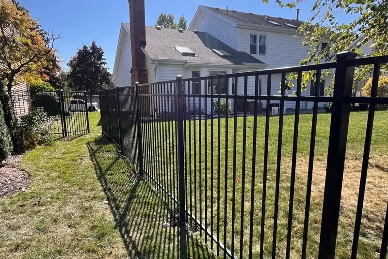 Black flat-top aluminum fence around a sunny yard beside a two-story home
