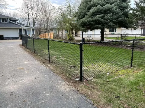 Black vinyl-coated chain-link fence beside a driveway
