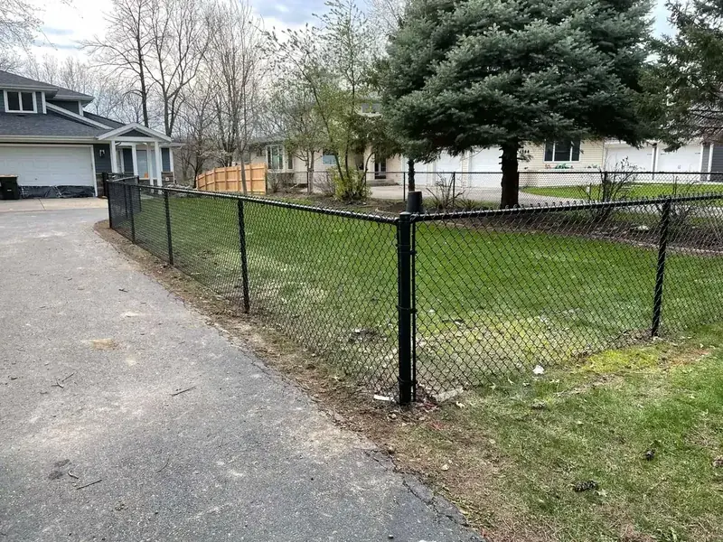 Black vinyl-coated chain-link fence enclosing a residential yard beside a driveway