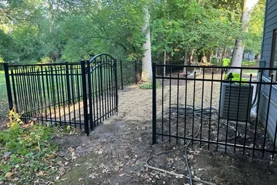 Black aluminum fence with an arched walk gate on a wooded lot