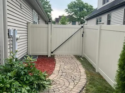 Tan vinyl privacy fence and matching gate framing a paver path